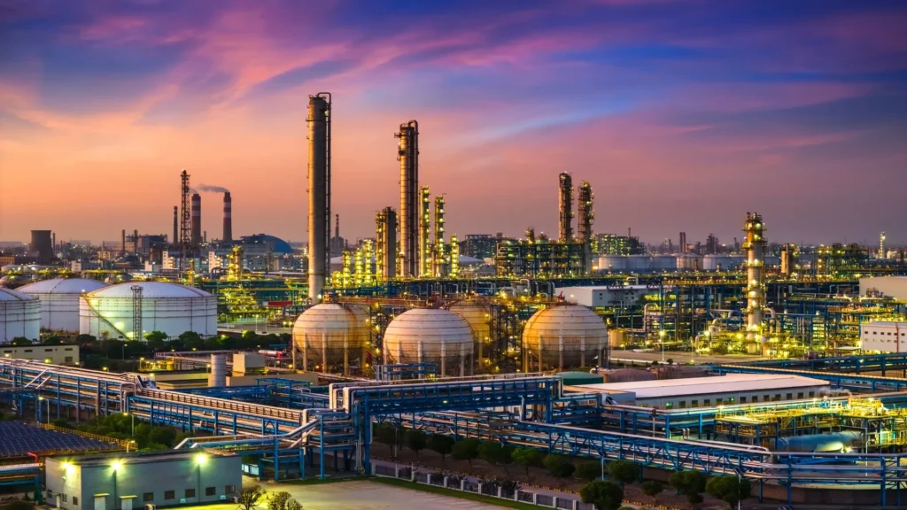 Refiner&iacute;a de petr&oacute;leo moderna con tanques de almacenamiento, tuber&iacute;as y torres de procesamiento al atardecer.