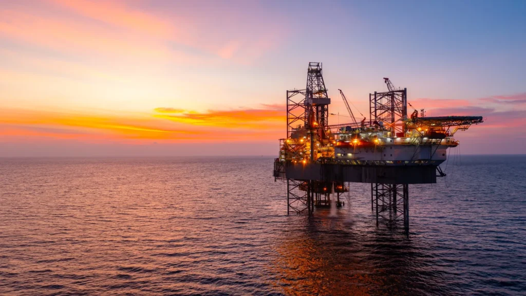 Plataforma de perforación offshore iluminada durante el atardecer, operando en medio del océano.