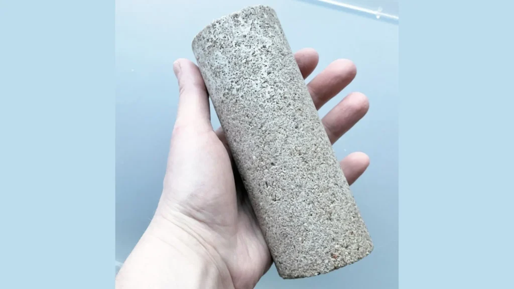 Cilindro de biohormigón sostenido por una mano, elaborado a partir de biomineralización con orina humana.