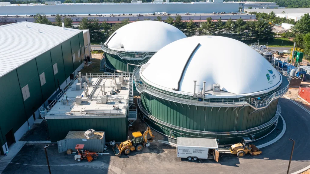 Vista aérea ilustrativa de instalaciones industriales tipo MORC con dos biodigestores circulares de techo blanco y maquinaria en primer plano, representando la tecnología de BTS Bioenergy.