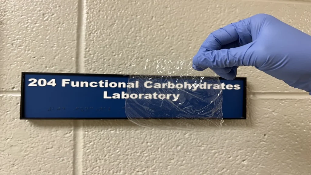 Investigador sostiene una película transparente de bioplástico para envases ecológicos elaborada a partir de cañas de vid, frente al laboratorio de carbohidratos funcionales de la Universidad Estatal de Dakota del Sur.