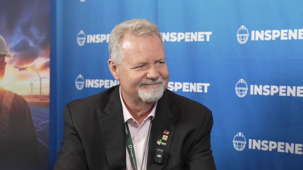 Clyde May, durante una entrevista en el evento ASNT 2025, con un fondo azul con el logotipo de INSPENET.