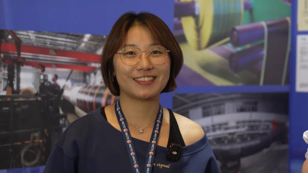 Wang Wei, ingeniera de ventas de VH-MARINETECH, sonr&iacute;e durante el evento SLOM 2025 mientras presenta las soluciones de mangueras flotantes de la empresa.