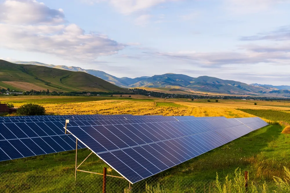 Energías renovables en acción: parque solar con paneles fotovoltaicos instalados en un campo abierto rodeado de colinas y cielo parcialmente nublado.
