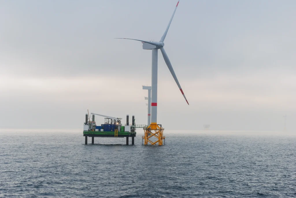 Plataforma offshore junto a aerogenerador en un parque eólico marino con cielo nublado.