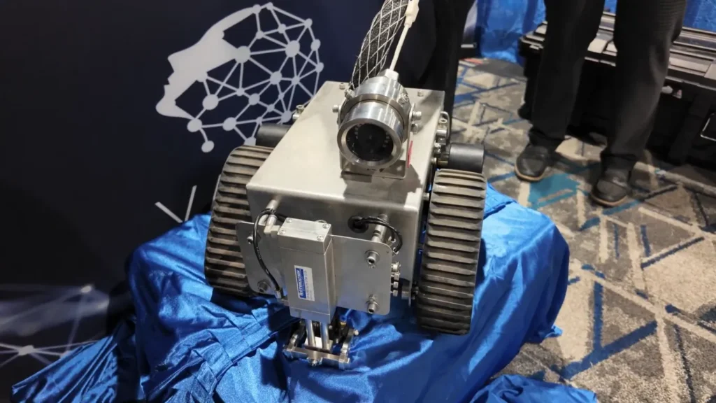 Robot PneuBot sobre una tela azul, con orugas de tracci&oacute;n y c&aacute;mara frontal, exhibido durante un evento industrial.