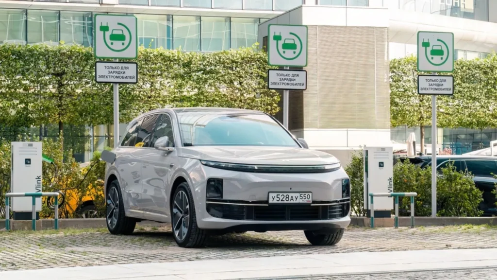 Estaci&oacute;n de carga en ciudad con veh&iacute;culo el&eacute;ctrico moderno, reflejando las ventas de veh&iacute;culos el&eacute;ctricos en expansi&oacute;n.