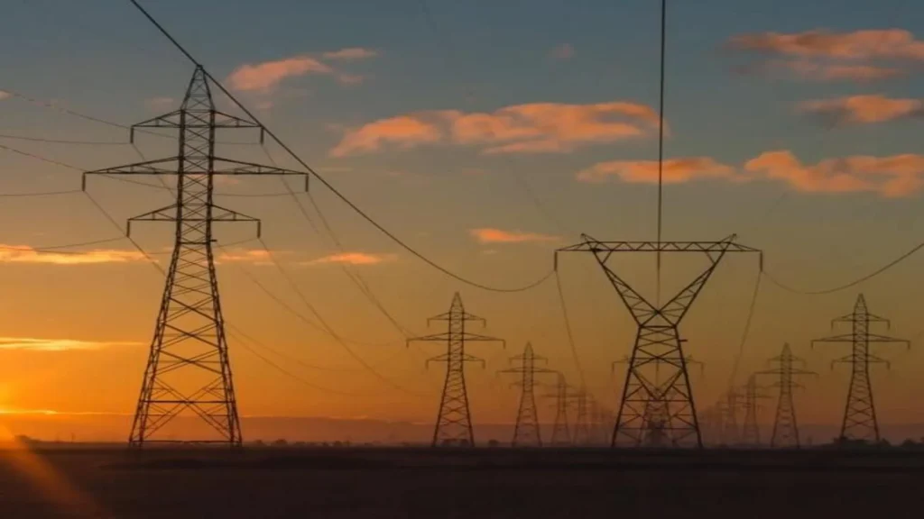 Torres de transmisi&oacute;n el&eacute;ctrica de GE Vernova al atardecer, conectadas por cables de alta tensi&oacute;n, con un cielo parcialmente nublado y tonos anaranjados.