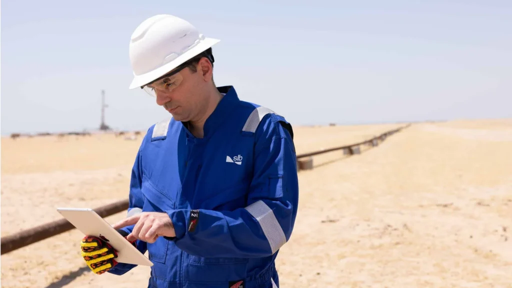 Trabajador con casco y ropa de seguridad azul utilizando una tableta en espacios del campo Mutriba asignado por SLB.