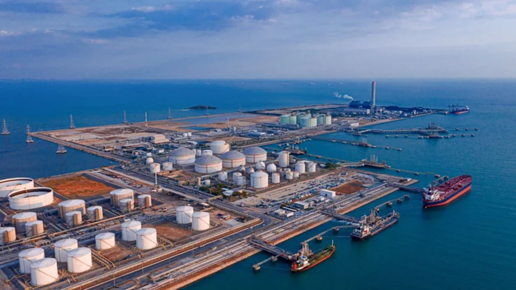 Gas crisis in India: maritime terminal with LPG storage tanks and cargo ships at a coastal energy facility.