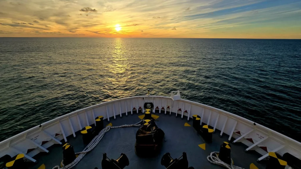 The *Fulmar Explorer* sailing on the open sea at sunset, with the vessel's bow facing the horizon during a marine exploration expedition in West Africa.